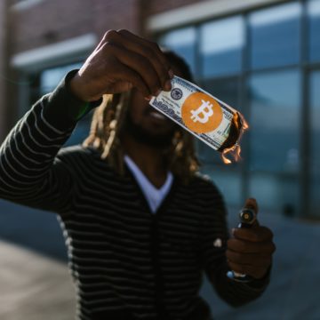 Mann zündet ein Geldschein mit Bitcoin Logo an