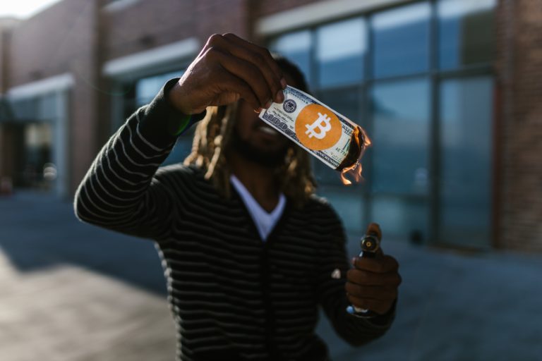 Mann zündet ein Geldschein mit Bitcoin Logo an