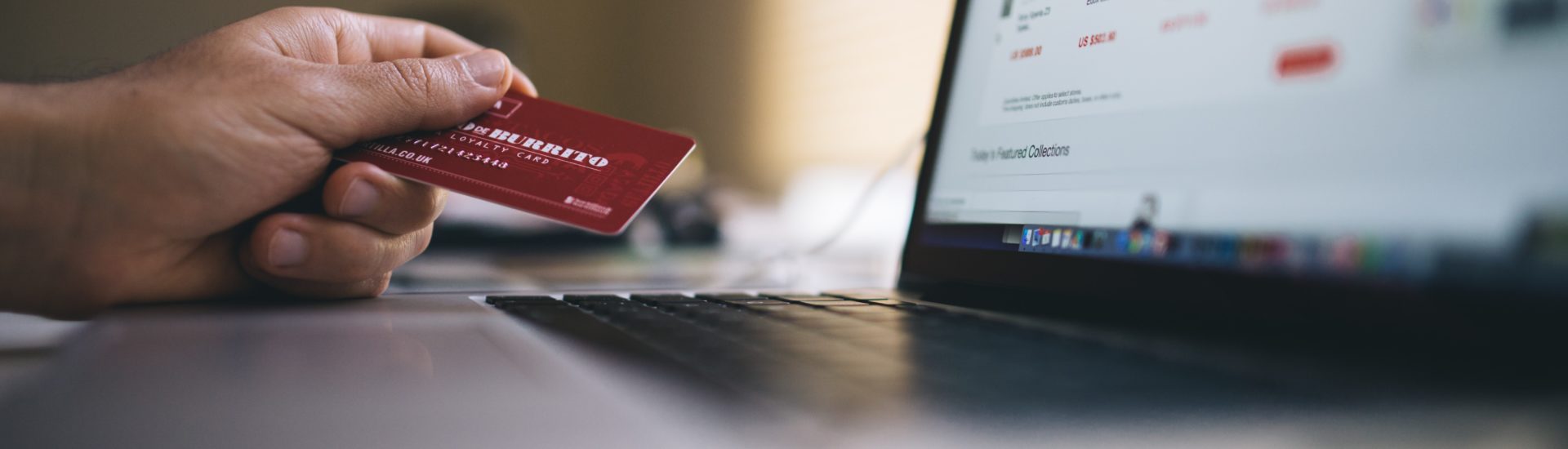 Person sitzt vor Laptop mit Kreditkarte in der Hand