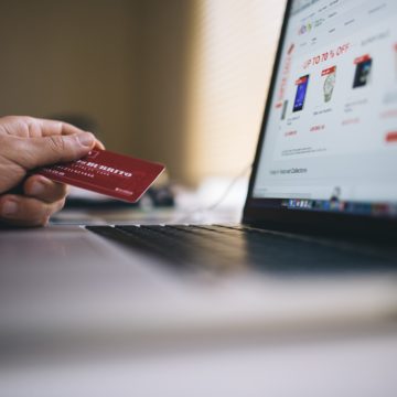 Person sitzt vor Laptop mit Kreditkarte in der Hand