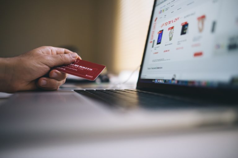 Person sitzt vor Laptop mit Kreditkarte in der Hand